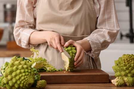 Woman cutting fresh Romanesco broccoli at table in kitchen, closeupの写真素材