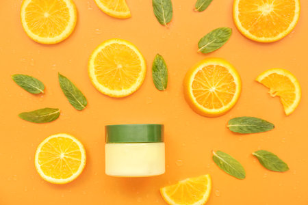 Jar of cosmetic cream with orange slices and mint on color backgroundの写真素材