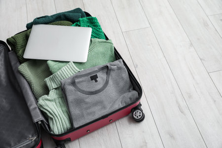 Open suitcase with laptop and sweaters on light wooden floorの写真素材