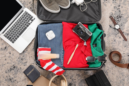 Suitcase with male clothes, laptop and travel accessories on color carpetの写真素材