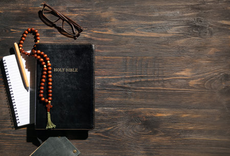 Holy Bible, notebooks, prayer beads, eyeglasses and pen on wooden background