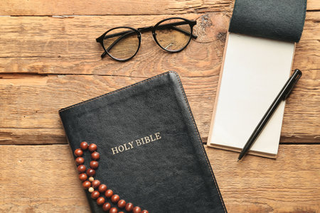 Holy Bible, prayer beads, notebook, pen and eyeglasses on wooden backgroundの写真素材