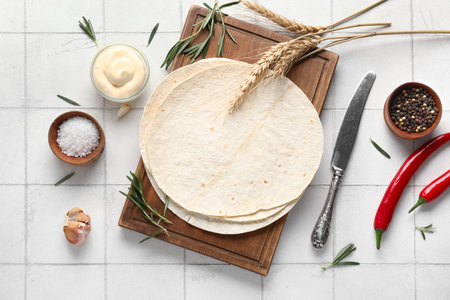Wooden board with fresh lavash, spices and sauce on white tile background