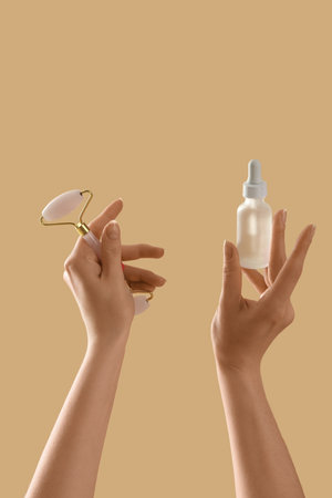 Hands holding cosmetic product and massage tool on beige backgroundの写真素材