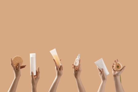 Hands holding cosmetic products and flower on beige backgroundの写真素材