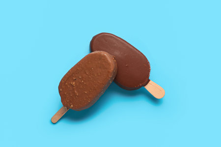 Delicious chocolate covered ice cream on stick against blue backgroundの写真素材