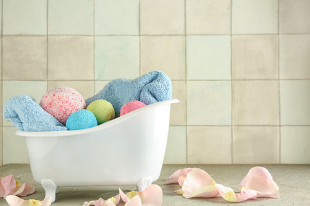 Little bathtub with bath bombs, towel and floral petals on table near tile wallの写真素材