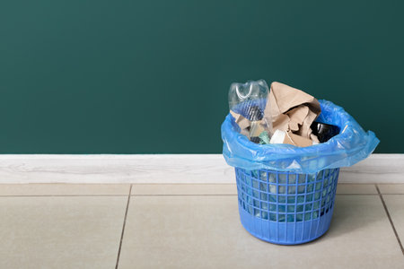 Trash bin with different garbage near green wallの写真素材