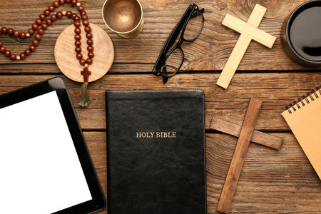 Holy Bible with prayer beads, tablet computer, eyeglasses and crosses on wooden background