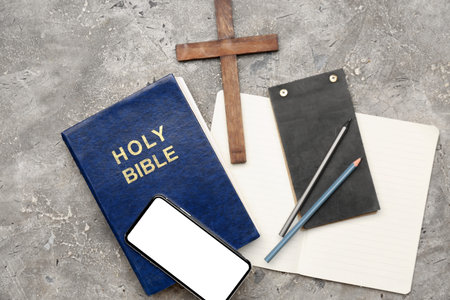Holy Bible with mobile phone, notebooks and cross on grunge background