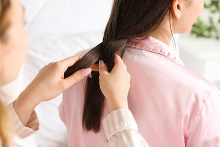 Young woman doing hair of her friend in bedroom, closeupの写真素材