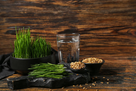 Fresh wheatgrass and glass of water on brown wooden tableの写真素材
