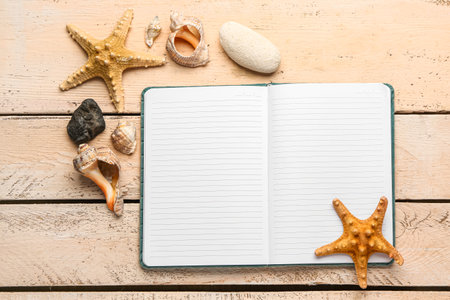 Open notebook with starfishes, shells and stones on beige wooden backgroundの写真素材