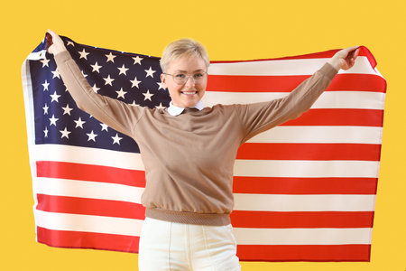 Young woman with USA flag on yellow backgroundの写真素材