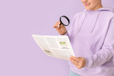 Young woman with magnifier reading newspaper on lilac background, closeupの写真素材