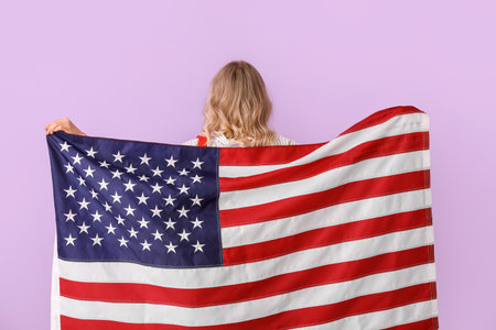 Young woman with USA flag on lilac background, back viewの写真素材