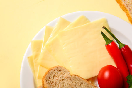 Plate of tasty processed cheese with bread and vegetables on yellow background