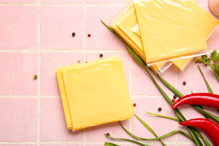 Slices of tasty processed cheese with scallions and chilli on pink tile background