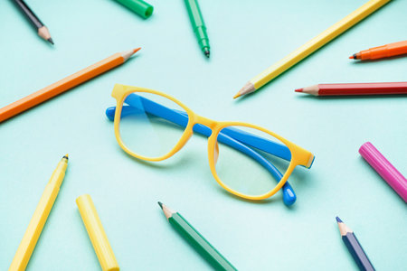 Stylish yellow eyeglasses with colorful pencils on pale turquoise backgroundの写真素材
