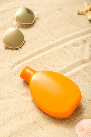 Creative composition with bottle of sunscreen cream with sunglasses on sand