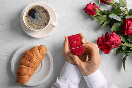 Man with engagement ring, coffee, croissant and roses on white background
