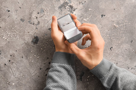 Man holding box with engagement ring on grunge background