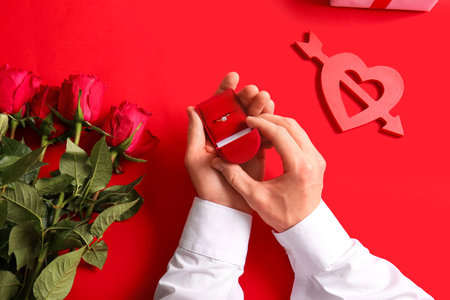 Man with engagement ring, roses and heart on red backgroundの写真素材