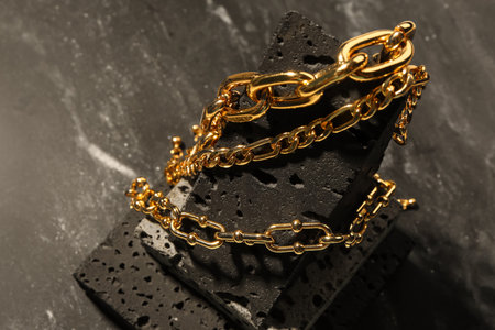 Decorative podium with beautiful chain bracelets on dark background