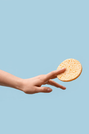 Hand with sponge for makeup removal on light blue background