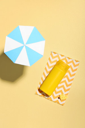 Creative composition with sunscreen and miniature umbrella on sand