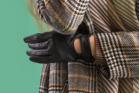 Beautiful woman in leather gloves and coat on green background, closeup