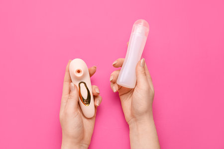 Woman holding vibrator and bottle of lubricant on pink backgroundの写真素材