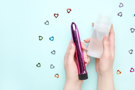 Woman holding vibrator and bottle of lubricant on blue background