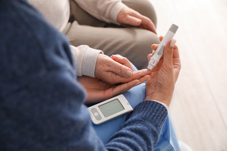 Young caregiver measuring sugar level of senior woman at home, closeup