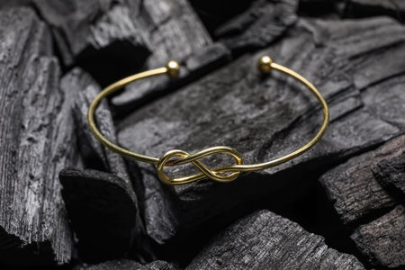 Golden bracelet on black charcoal, closeup
