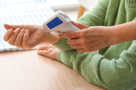 Young caregiver measuring temperature of senior woman with infrared thermometer in kitchen, closeupの写真素材