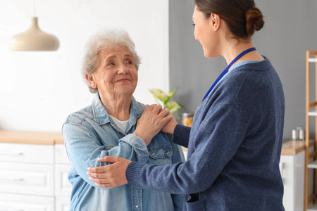 Young caregiver with senior woman hugging in the kitchenの写真素材