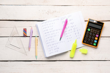 Copybook with maths formulas, calculator and stationery on white wooden tableの写真素材