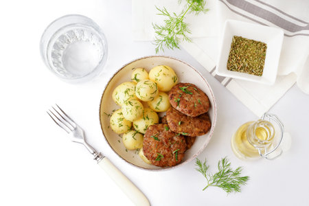 Bowl with cutlets, boiled baby potatoes and dill on white table in kitchenの写真素材