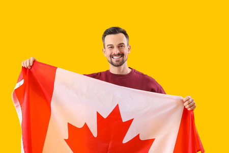 Handsome man with flag of Canada on yellow backgroundの写真素材