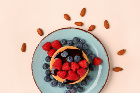 Plate with sweet pancakes, berries and nuts on beige backgroundの写真素材
