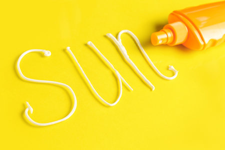 Bottle with sunscreen and word SUN made of cream on yellow backgroundの写真素材