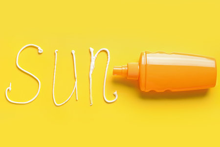 Bottle with sunscreen and word SUN made of cream on yellow backgroundの写真素材