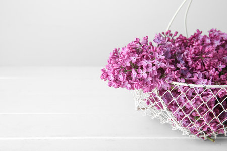 Basket with beautiful lilac flowers on wooden table near white wallの写真素材