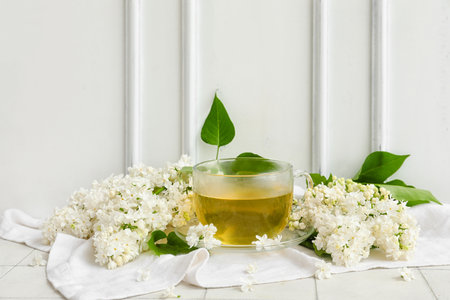 Cup of tea and lilac flowers near white wooden wallの写真素材