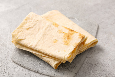Board with fresh lavash on gray background