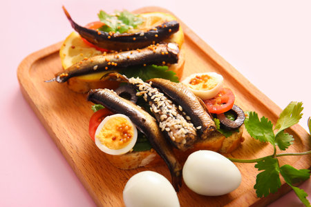 Wooden board of tasty sandwiches with canned smoked sprats on pink backgroundの写真素材