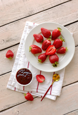 Plate with fresh strawberries and jam on white wooden backgroundの写真素材