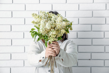 Young woman with bouquet of lilac flowers on white brick wall background