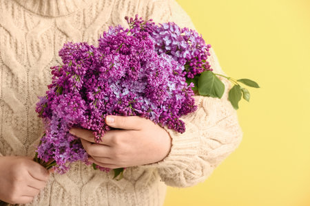 Young woman with bouquet of lilac flowers on yellow backgroundの写真素材